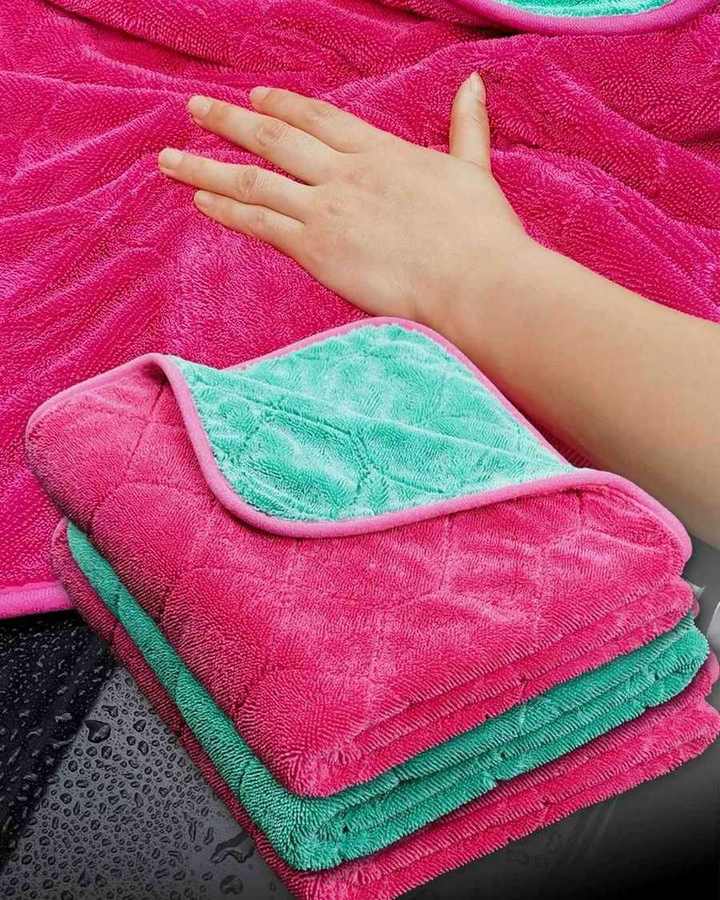 Pink twist loop towel spread under a hand, with a folded towel in front showing the teal side