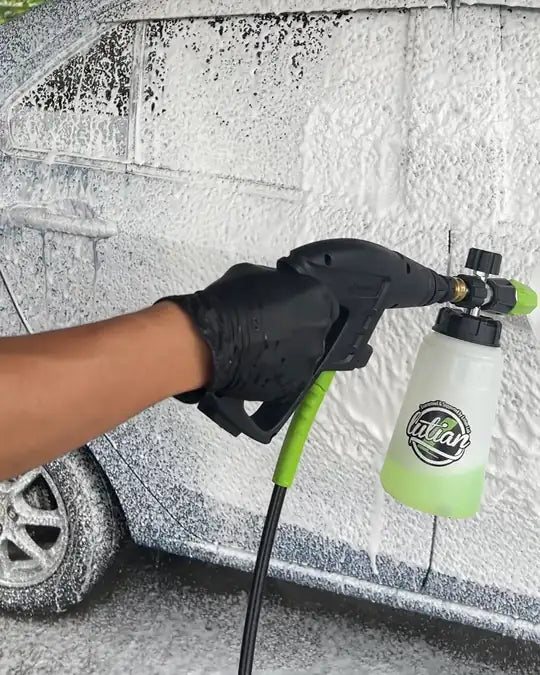 A gloved hand on the green hose and the foam pot, a car under foam